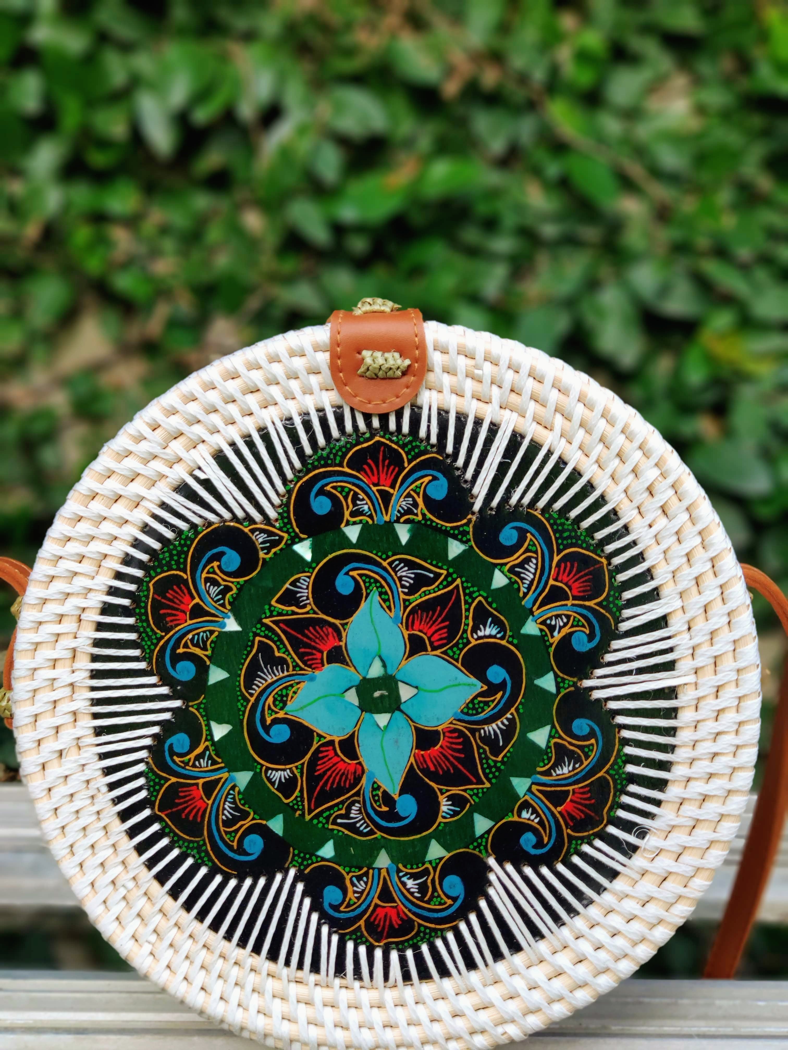 Round woven bag with colorful floral design on a green leafy background